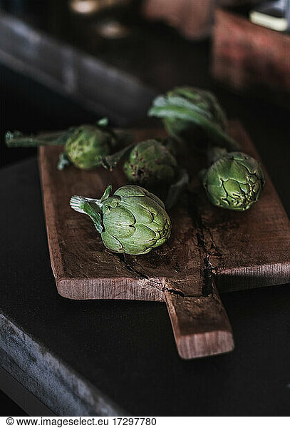 Fresh green baby artichokes on wooden cutting board on kitchen counter