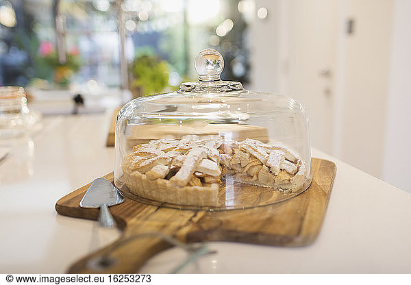 Fresh homemade apple pie under cake dome on cutting board