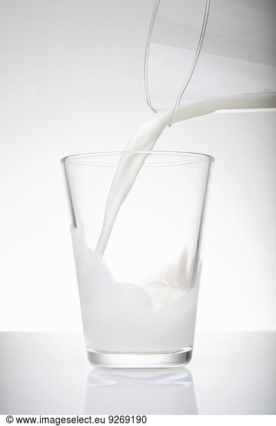 Fresh milk pouring from jug into drinking glass