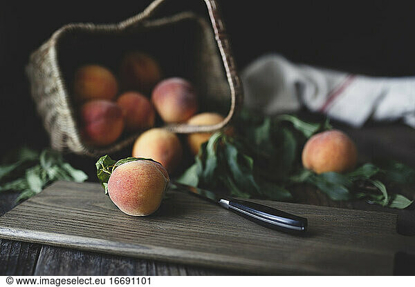 fresh peaches in tipped basket and on cutting board with knife