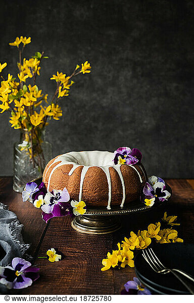 Freshly baked bundt cake on stand decorated with flowers.