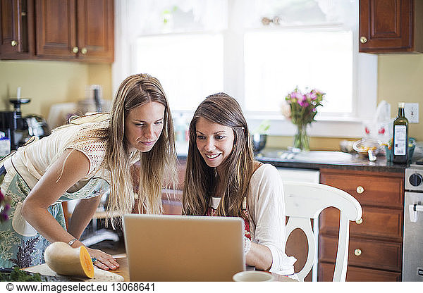 Freunde benutzen Laptop-Computer  während sie zu Hause Essen zubereiten