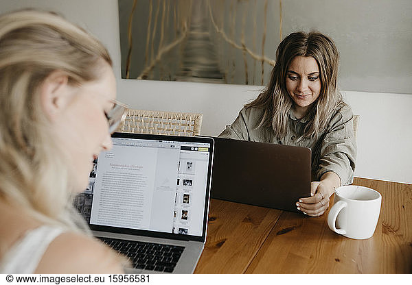 Freunde  die an Laptops arbeiten  während sie während der Sperre im Heimbüro am Tisch sitzen