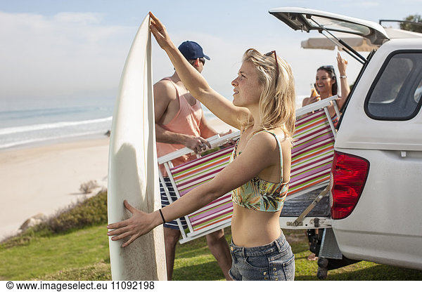 Freunde  die Surfbrett und Strandkorb aus dem Auto an der Küste nehmen.