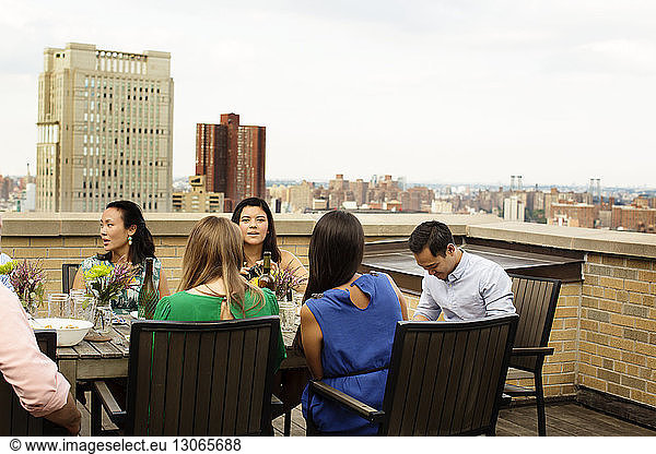 Freunde essen bei Tisch auf der Gebäudeterrasse bei klarem Himmel