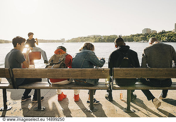 Freunde essen Essen auswärts,  während sie an sonnigen Tagen nebeneinander auf einer Bank in der Stadt sitzen
