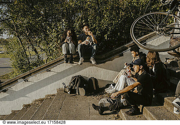 Freunde mit Essen und Trinken beim Sitzen auf Stufen im Park