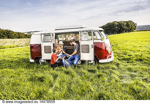 Freunde picknicken in einem Lieferwagen  der auf einem Feld in ländlicher Landschaft geparkt ist