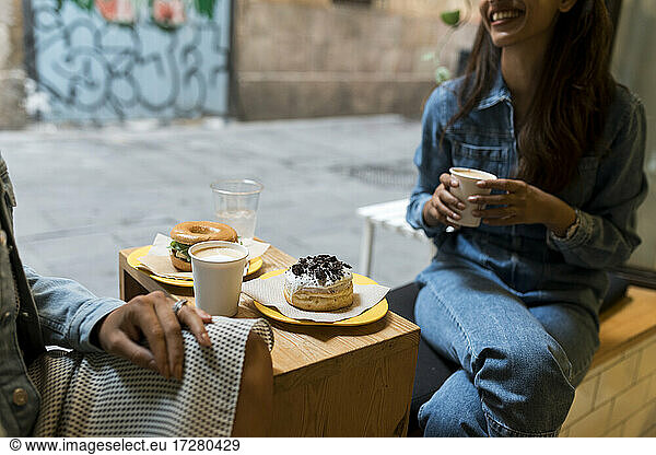 Freunde trinken Kaffee und essen  während sie am Fenster eines Cafés sitzen