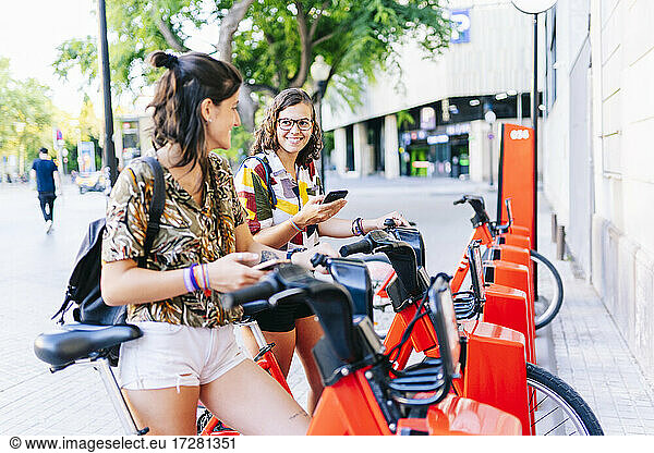 Freundinnen benutzen ein Handy  während sie an einer Fahrradabstellanlage stehen