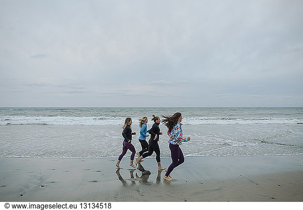 Freundinnen  die am Strand gegen den Himmel joggen  während sie am Strand trainieren
