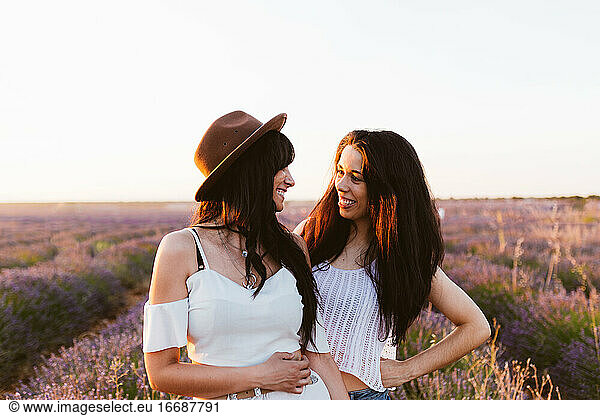 Freundinnen  die sich lächelnd in einem Lavendelfeld anschauen