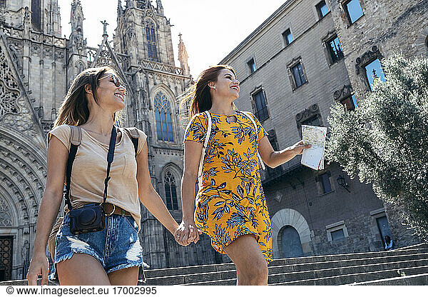 Freundinnen halten sich an den Händen  während sie gegen den Platz der Kathedrale von Barcelona in Barcelona  Katalonien  Spanien  laufen