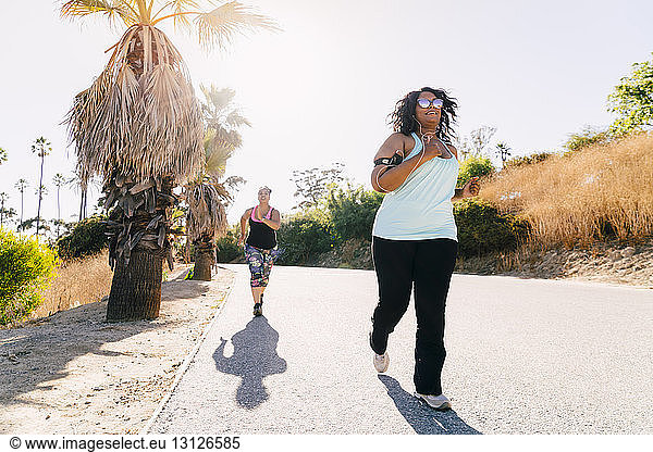 Freundinnen joggen bei Sonnenschein auf der Straße bei klarem Himmel