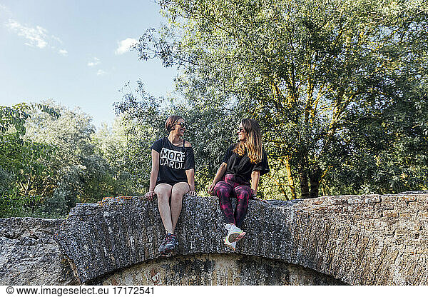 Freundinnen sitzen auf alter Mauer gegen Bäume