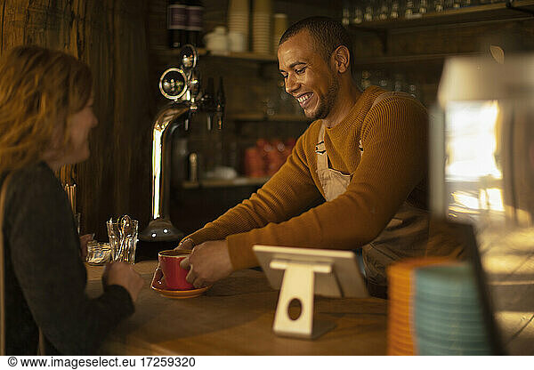 Friendly barista serving coffee to excited woman at cafe counter
