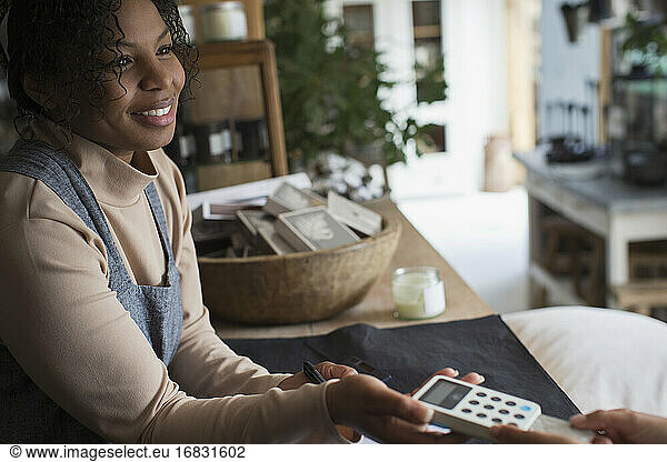 Friendly female shop owner holding credit card reader for customer