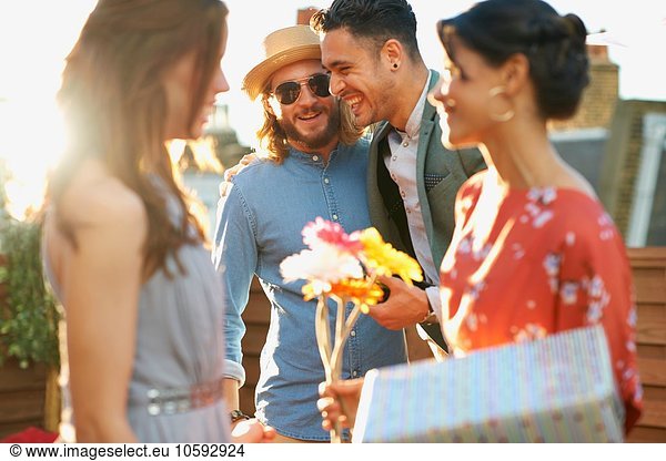 Friends at party on roof terrace holding flowers and gift smiling
