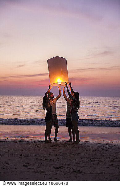 Friends burning paper lantern standing at beach on sunset