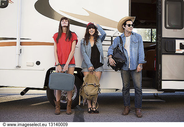 Friends carrying luggage while standing against camper van