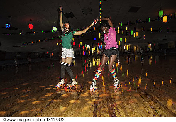 Friends dancing while roller skating at illuminated roller rink