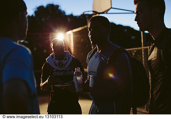 Friends discussing while standing in basketball court at dusk