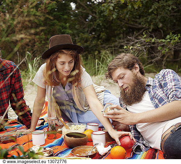 friends having breakfast while relaxing on field in forest