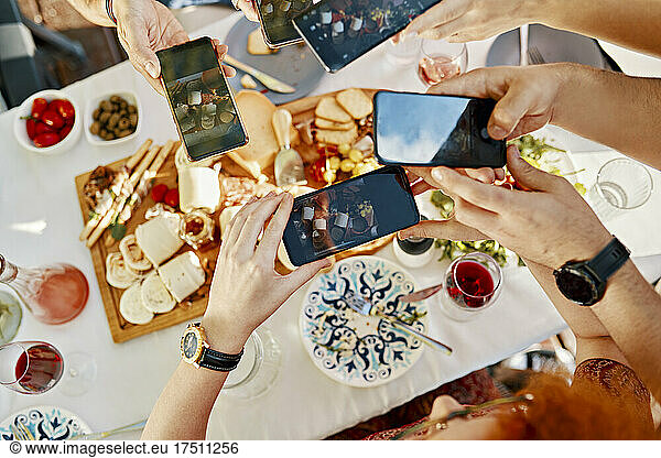 Friends having dinner with a cheese platter taking smartphone pictures