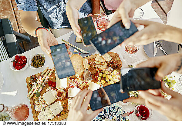 Friends having dinner with a cheese platter taking smartphone pictures