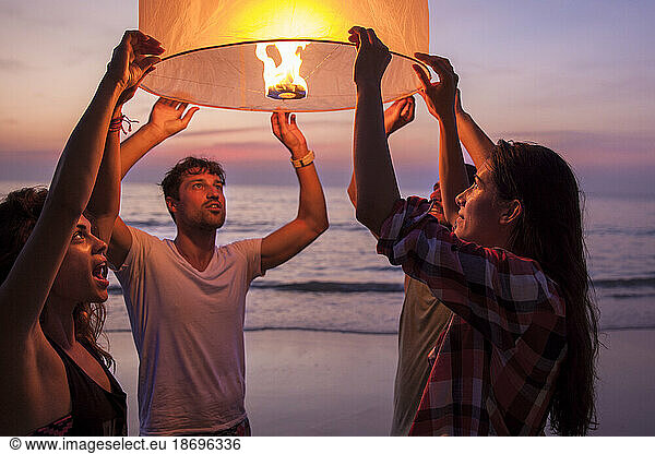 Friends holding lit paper lantern at beach