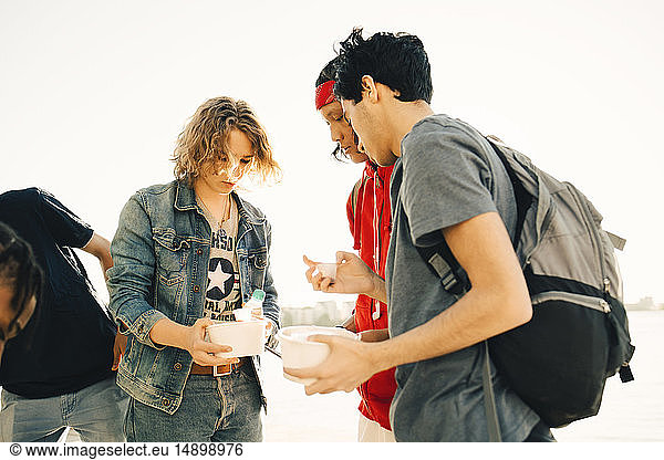Friends holding take out food while standing on promenade in city during sunny day