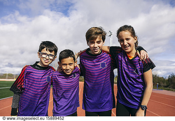 Friends in a sports team standing on running track with arms around