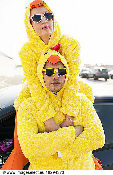 Friends in sunglasses and yellow chicken costumes in front of car