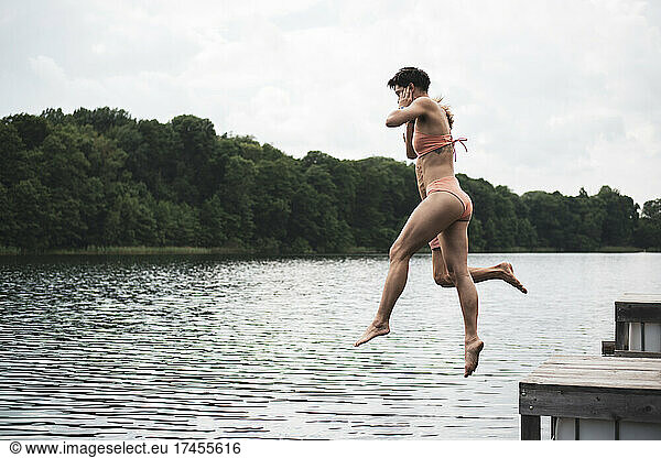Friends jumping in lake in Poland in orange swimsuit in summer