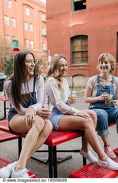 Friends laughing while sitting on picnic table with coffees