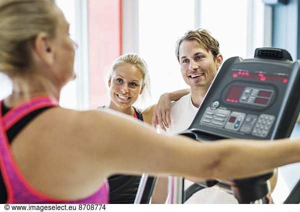 Friends looking at woman exercising on treadmill at gym