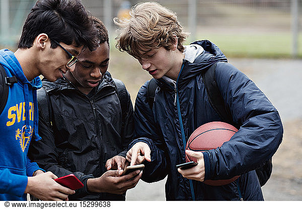Friends looking in teenage boy's phone while standing with ball on playing field