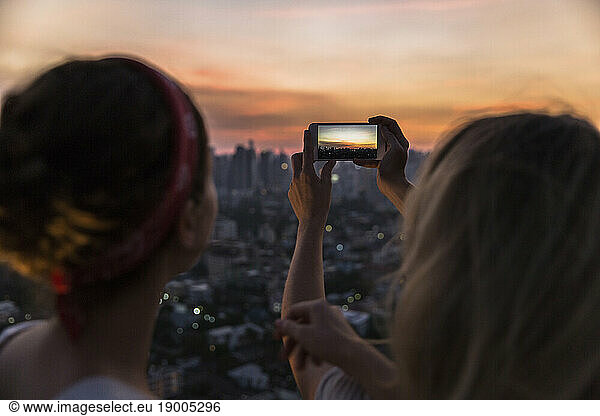 Friends photographing city view through smart phone at dusk