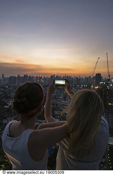 Friends photographing city with sky at dusk