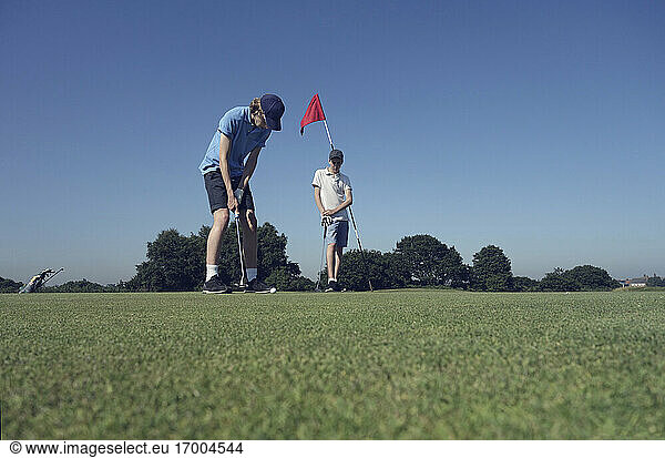 Friends playing golf against clear blue sky on course