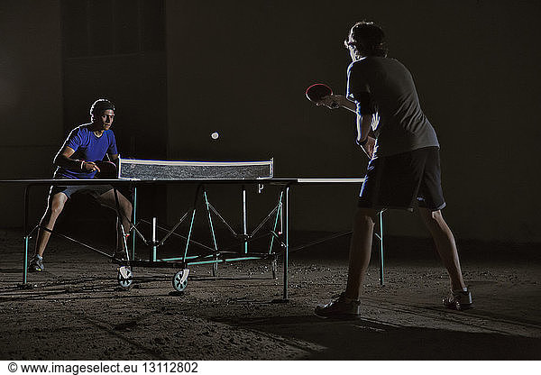 Friends playing table tennis against building at night