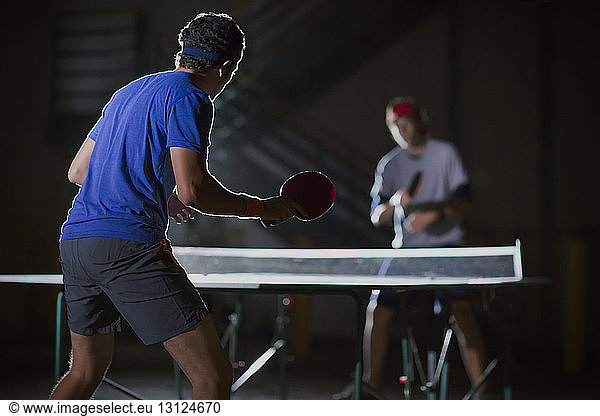 Friends playing table tennis against illuminated building
