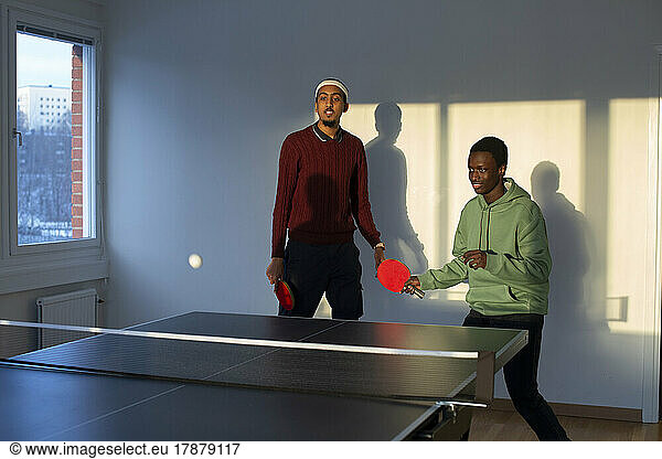 Friends playing table tennis in games room