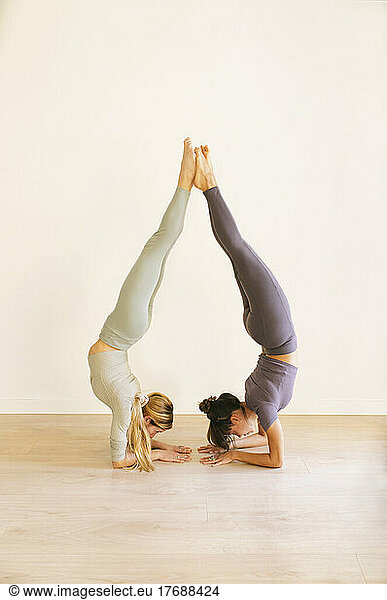 Friends practicing handstand pose by wall at yoga studio