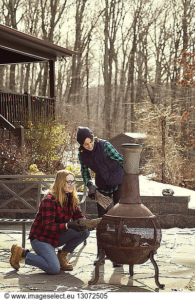 Friends putting firewood in fire pit