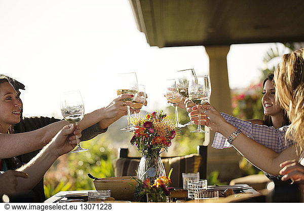 Friends raising toast while sitting at dining table on porch