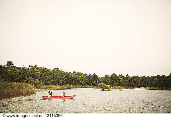 Friends rowing boat in lake against sky