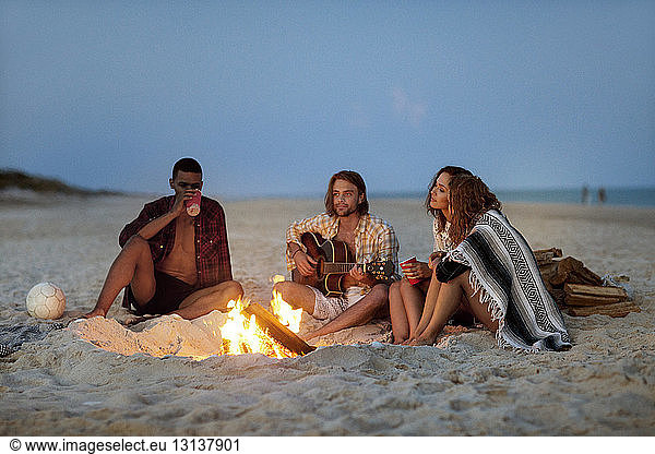 Friends sitting by bonfire at beach
