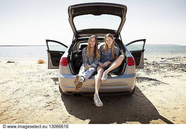 Friends sitting in car trunk against beach