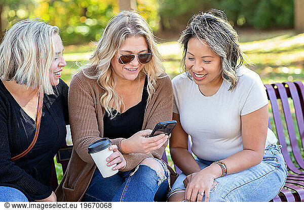 Friends sitting on a bench looking at a phone